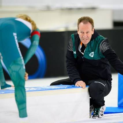 Erik Wink steekt zijn hand uit om zijn schaatser te prijzen